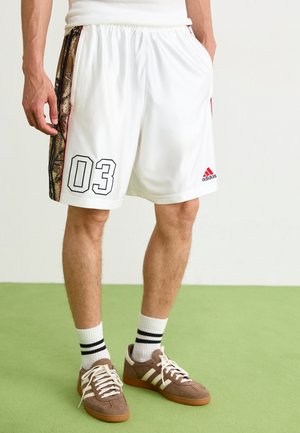 Balti sportiniai šortai su kamufliažo šonine juostele, su juodu spaudiniu "03" ir raudonu Adidas logotipu. Lygus paviršius, elastinė juostos juosta.