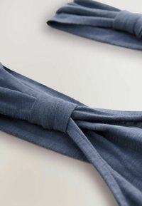 Bandeau aus blauer Stoff mit einem verknoteten Design und weicher, strukturierter Oberfläche, das ein glattes, leichtes Material zeigt.