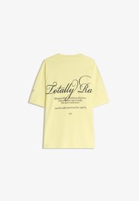 Tricou galben din bumbac cu mâneci scurte, cu text mare negru pe spate, inclusiv "Totally Ra" și fraze adiționale dedesubt.
