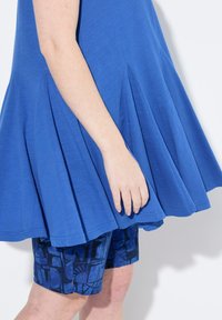 Tunic blu plettata con una texture morbida abbinata a pantaloni shorts blu a fantasia con forme geometriche.