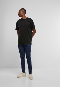 Camiseta negra de manga corta, corte holgado, combinada con jeans ajustados azul oscuro y zapatillas color crema. Diseño simple, sin patrones ni logotipos visibles.