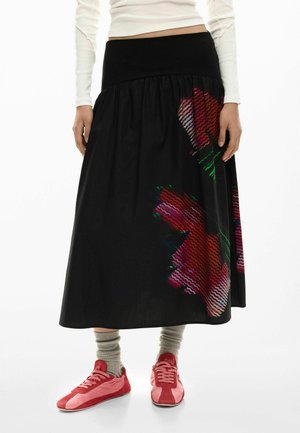 Black skirt with a gathered design, featuring a colorful abstract floral pattern on one side. Worn with red shoes and gray socks.