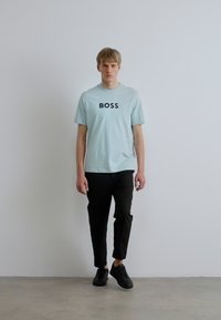 Heleroheline T-särk musta "BOSS" tekstiga, ühendatud mustade kitsenevate pükste ja mustade tossudega. Sile tekstuur, vabaaja disain, täis kehapilt.