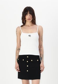 Hvit ribbet tanktop med smale stropper, prydet med et lite svart grafikkmotiv. Kombinert med et svart miniskjørt med gullknappdetaljer.