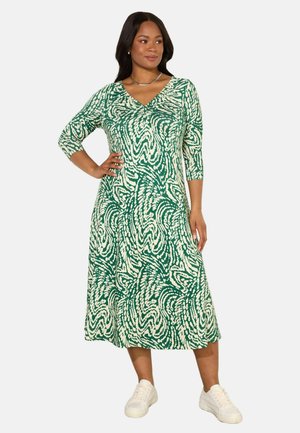 Groene en witte jurk met patroon, een V-hals, driekwart mouwen en een vloeiende silhouet, gecombineerd met witte sneakers.