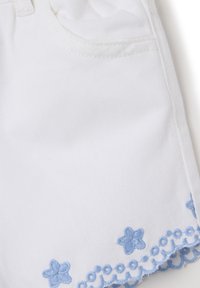 Pantalones cortos de mezclilla blanca con bordado floral de color azul claro y detalle de encaje en forma de ondas en el dobladillo. Presenta un bolsillo frontal y un tejido texturizado.