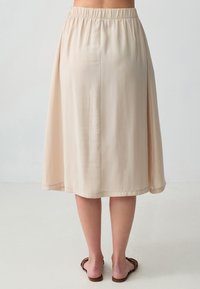 Jupe beige, de longueur genou, faite d'un tissu lisse ; présente une taille élastique et une silhouette évasée. Pas de motifs visibles ni de matériel apparent.