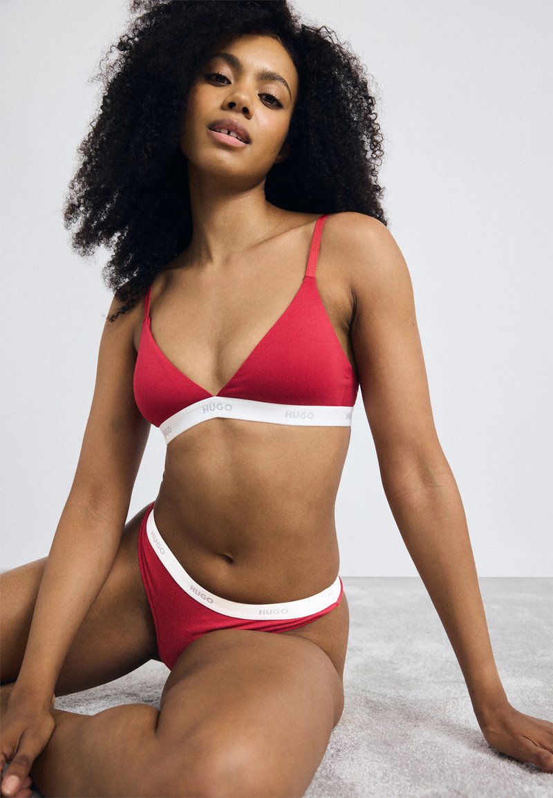 Rode lingerieset met een driehoekige bralette en bijpassende slip. Witte elastische band met "HUGO" logo op de taille en onder de buste. Gladde textuur.