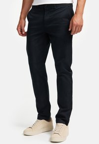 Navyblaue Chinos aus einem Baumwoll-Mix, Slim Fit, mit Knopfverschluss und Seitentaschen, kombiniert mit hellbeigen Sneakern.