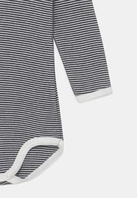 Dlhý rukáv bodysuit s námorníckymi a bielymi horizontálnymi pruhmi, vyrobený z mäkkého materiálu s cvokmi a bielou obrubou na okrajoch.