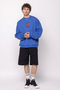 Zils pārklāts džemperis ar grafisku drukājumu, melni šorti, balti zeķes ar ziliem svītrām un melni augstie apavi.