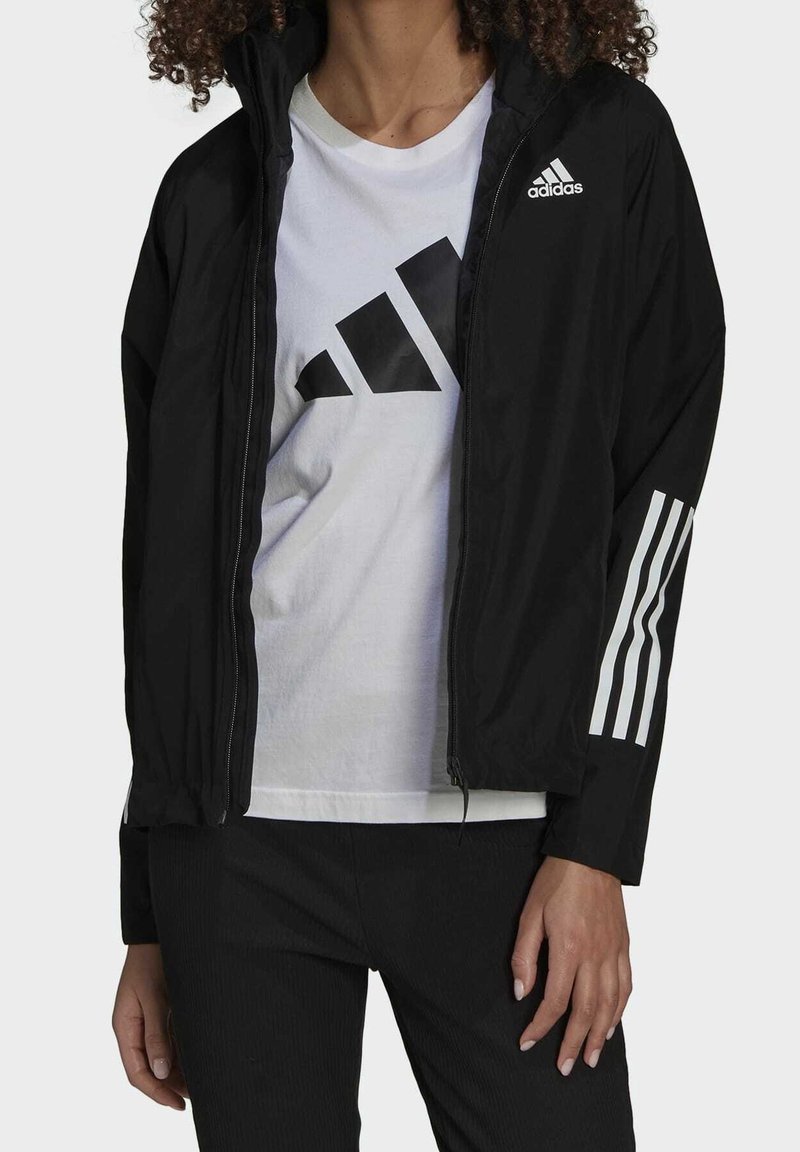 Giacca leggera nera con zip frontale, presenta il logo Adidas sul petto e tre strisce bianche sulle maniche.