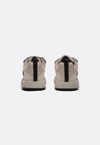 Zapatillas beige con un upper de tejido texturizado, acentos negros y un collarín acolchado en el tobillo, que cuentan con una suela de goma para mayor agarre.