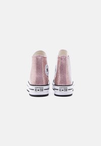 Ζευγάρι ροζ γκλίτερ ψηλά αθλητικά παπούτσια Converse All Star, εμφανιζόμενα από πίσω, πάνω σε λευκό φόντο.