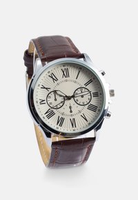 Brūna ādas siksna, sudraba krāsas korpuss, krēmveida teksturēts ciparnīca, melni romiešu cipari un divi apakšciparnīcas papildu funkcionalitātei.