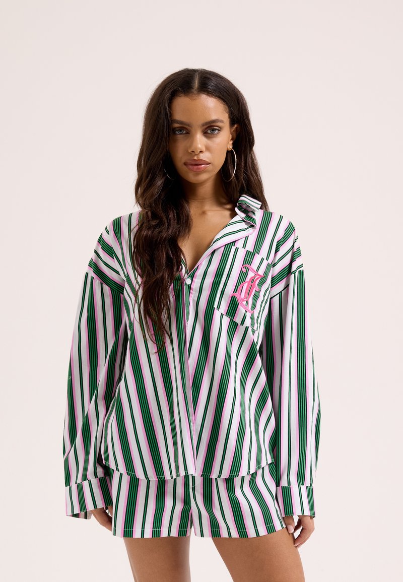 Femme aux longs cheveux foncés portant une chemise de pyjama rayée verte, rose et blanche et un short assorti avec un monogramme rose sur la poche.