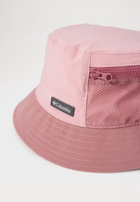 Pink bucket hat made from lightweight fabric, featuring a textured top with a zip pocket and a solid brim, branded with a black logo.