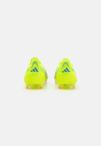 Botas de fútbol amarillas brillantes con parte superior sintética texturizada, tachuelas transparentes rosas y detalles en azul en el talón.