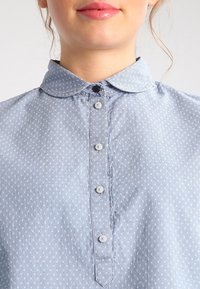 Ljusblå skjorta med krage och prickigt mönster, med knäppning framtill med ljusa knappar och en mjuk, texturerad tyg.