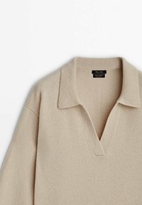 Pull en laine et cachemire beige avec un large col et un détail en V au niveau du col, montrant la moitié supérieure du vêtement.