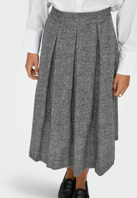 Pelēka plisēta svārki izgatavoti no teksturēta auduma, līdz ceļgaliem, ar elastīgu jostasvietu. Apvienoti ar melniem loafers un baltu kreklu.