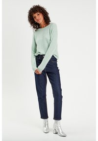 Suéter verde claro y suave de manga larga, combinado con jeans de mezclilla azul oscuro. El modelo lleva botines plateados brillantes con tacón cuadrado.