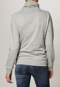 Felpa grigia con colletto alto, realizzata in tessuto morbido. Presenta polsini e orlo a costine, con un design aderente che mostra tasche.