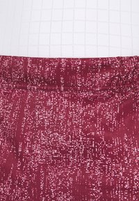 Bordeauxfärgade tygshorts med ett texturerat, abstrakt mönster. Har en elastisk midja och en subtil glans. Stilen prioriterar komfort och flexibilitet.