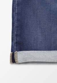 Jeansfabric med avskuren fåll och en mörkblå utsida samt en ljusblå insida. Har beige sömmar och en ren finish.