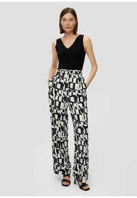 Pantalons taille haute noirs et blancs à motif avec une coupe ample, dotés de poches latérales et associés à un haut sans manches noir.