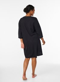 Svart, knälång klänning i lätt tyg. Har trekvartslånga ärmar och en avslappnad passform med rund halsringning.