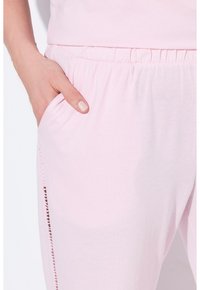 Světle růžové pyžamové kalhoty vyrobené z měkké tkaniny, mají elastický pas a boční kapsu s dekorativním šitím.