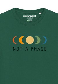 Donkergroene t-shirt met een meerkleurige maanfase afbeelding boven de tekst "NOT A PHASE" in zwart. Katoenen materiaal, ronde hals ontwerp.