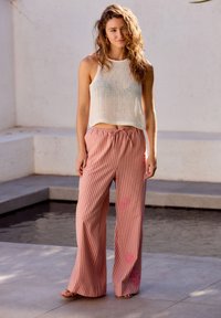 Cropped top bianco in maglia abbinato a pantaloni a gamba larga a righe rosa e bianche con accenti floreali rosa, ideale per un look informale.