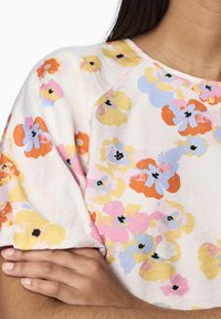 Blommönstrad topp med flerfärgade blommor i rosa, gult och blått på en ljus bakgrund. Mjuk tyg med en avslappnad passform.