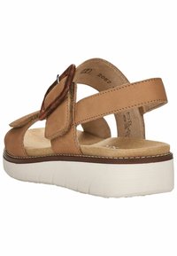 Sandal in pelle marrone con cinturini regolabili, un accento circolare, soletta morbida e suola piattaforma bianca con scanalature testurizzate.