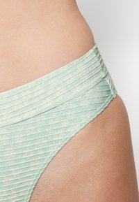 Parte de baixo de biquíni verde menta com uma textura canelada, apresentando um padrão floral em tons mais claros. A cintura é larga e elástica.