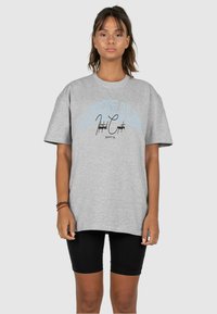 Gray cotton T-shirt with a loose fit, featuring blue and black text graphics. Paired with black bike shorts for a casual look.