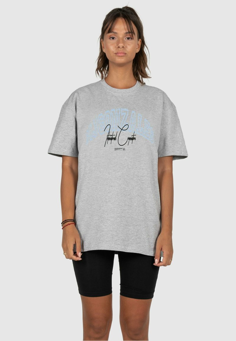 Gray cotton T-shirt with a loose fit, featuring blue and black text graphics. Paired with black bike shorts for a casual look.