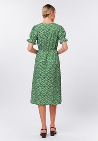 Grünes Blumenkleid mit Puffärmeln, knieumspielend, tailliert, aus leichtem Stoff. Verfügt über kleine weiße Blumenmuster.