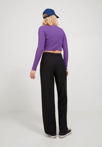 Violetti, pitkähihainen lyhyt paita yhdistettynä mustiin, korkeavyötäröisiin, leveälahkeisiin housuihin ja mustiin tennareihin, nähtynä takaa.