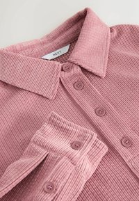 Rosa Cord-Stoffhemd mit kragenförmigem Ausschnitt, ausgestattet mit vier Knöpfen an der Vorderseite und eingeknöpften Ärmeldetails; weiche Textur und geripptes Muster.