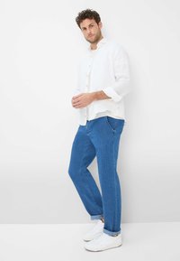 Camicia bianca in lino con bottoni, pantaloni in denim blu e sneakers bianche. La camicia ha una vestibilità morbida; i pantaloni hanno tasche laterali e un design a gamba dritta.