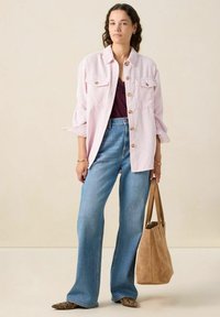 Lichtroze gestreepte oversized shirt, donkere tanktop eronder, hooggeplaatste blauwe spijkerbroek, bruine suède schoudertas en gebloemde ballerina's.