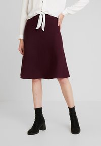 Burgundy a-linjekjol med texturerad yta, tillsammans med en vit blus med knytfram. Bärs med svarta klackade ankelstövlar.