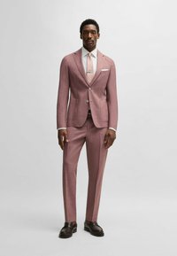 Lichtroest pak met een gecreëerde afwerking, gecombineerd met een witte blouse en een bijpassende stropdas. Donkerbruine schoenen maken de formele look compleet.