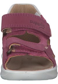 Rosa velcro-sandal med utskurne mönster, mjukt läderöverkänsla, vadderat innertyg och vit gummisula. Har branding på remmen.