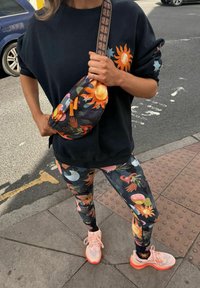 Musta ylikokoinen collegepaita, jossa aurinkokuosi, kuvioidut leggingsit, joissa on kukkaisia muotoja, ja vaaleanpunaiset tennarit oransseilla yksityiskohdilla.