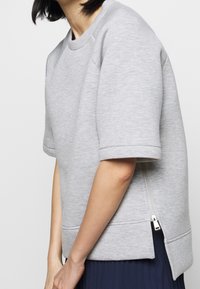 Šedá oversized mikina vyrobená z měkké látky, s krátkými rukávy a zipem po bočním švu. Jednoduchý design s čistým provedením.