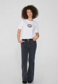 Camiseta blanca de manga corta con un diseño de labios de estampado de leopardo, combinada con unos jeans negros de campana y un cinturón negro con una hebilla dorada.